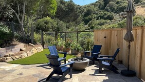Eine Terrasse im Freien mit Steinboden, einem Feuerkorb und Adirondack-Stühlen.