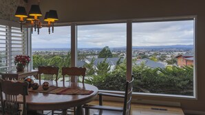 Ein Essbereich mit Tisch, Stühlen und Blick auf eine Stadtlandschaft durch große Fenster.
