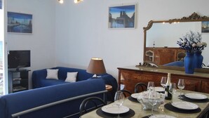 Habitación de hotel con un sofá azul, una mesa de comedor con platos y vasos, una lámpara y un espejo.