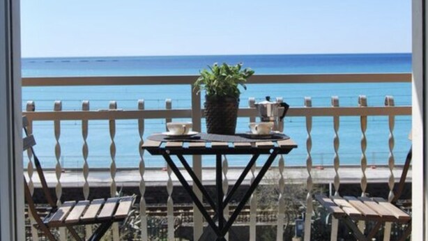 Un balcón con vista al mar, una mesa con una planta y dos sillas.