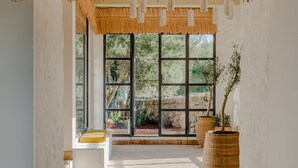 Ruime binnenruimte met betegelde vloer, een trap naar een balkon en een groot raam met uitzicht op groen.