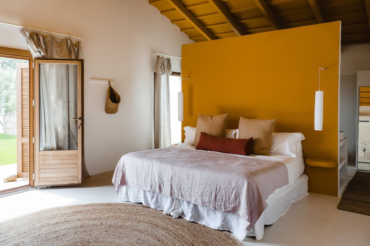 A bedroom with a bed, a wooden ceiling, a white wall, and a yellow accent wall.