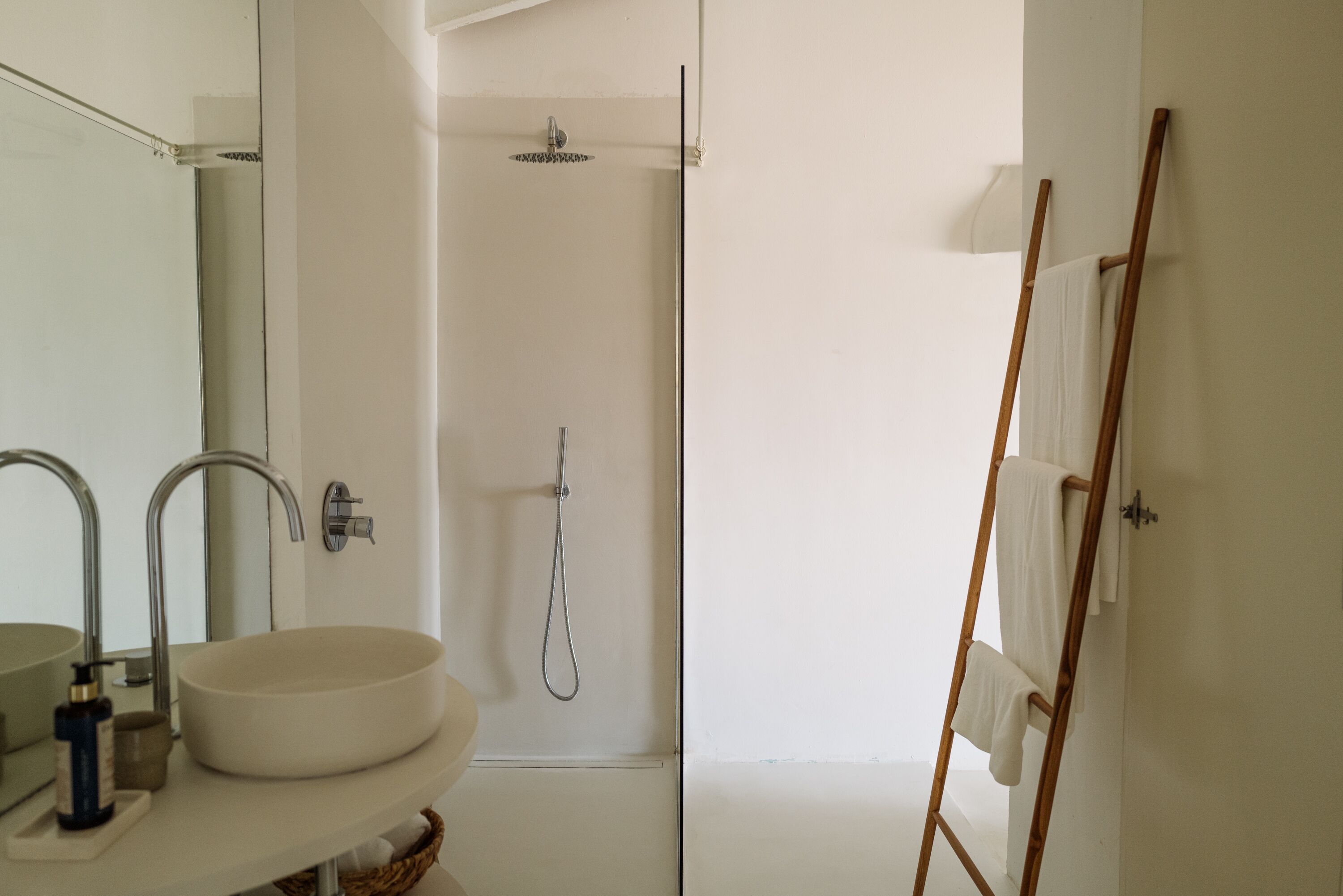 Un baño con un lavamanos grande, dos espejos, una ducha y una escalera de madera.