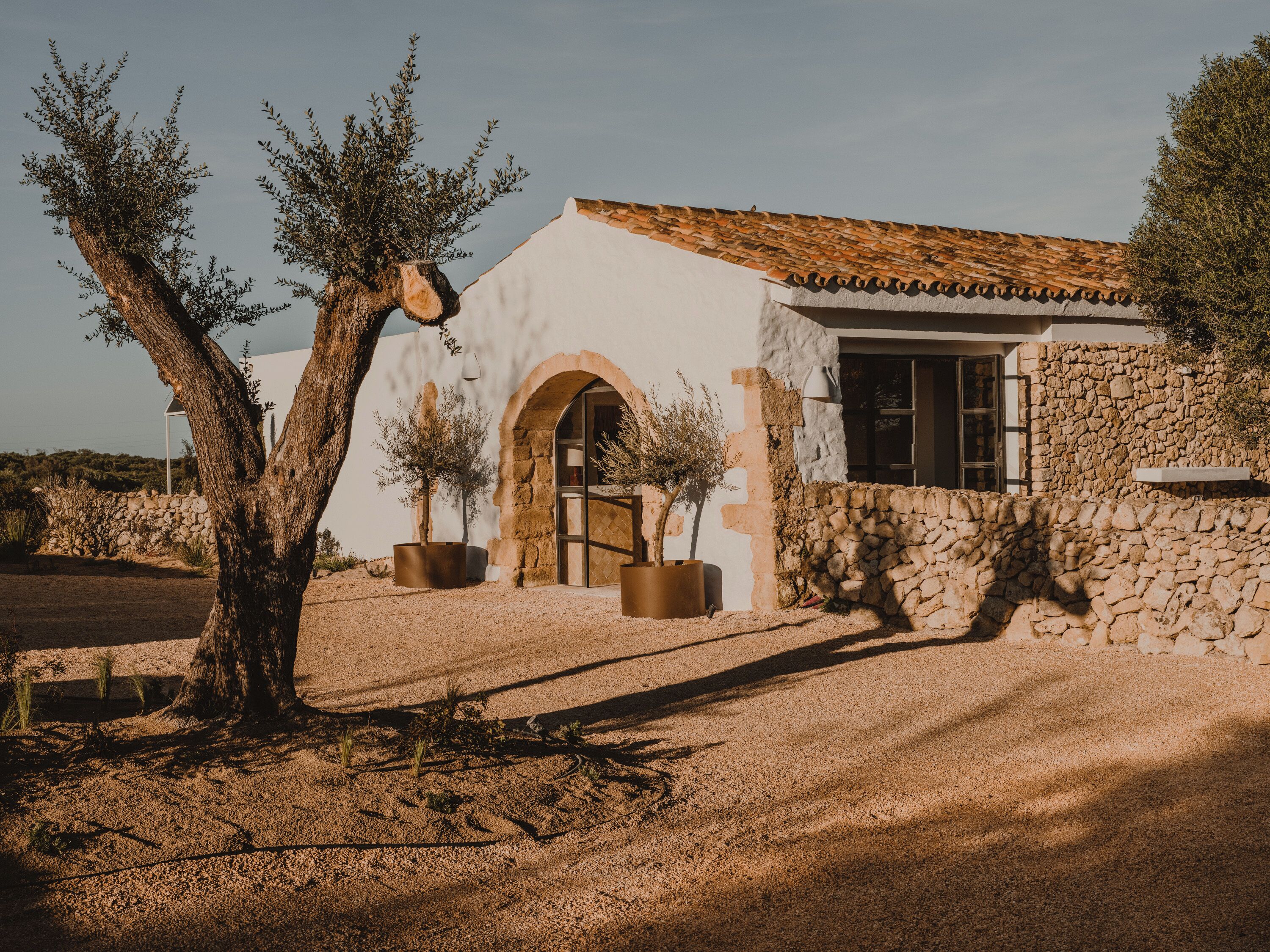 A rustic building with a stone facade, an arched doorway, and potted plants.