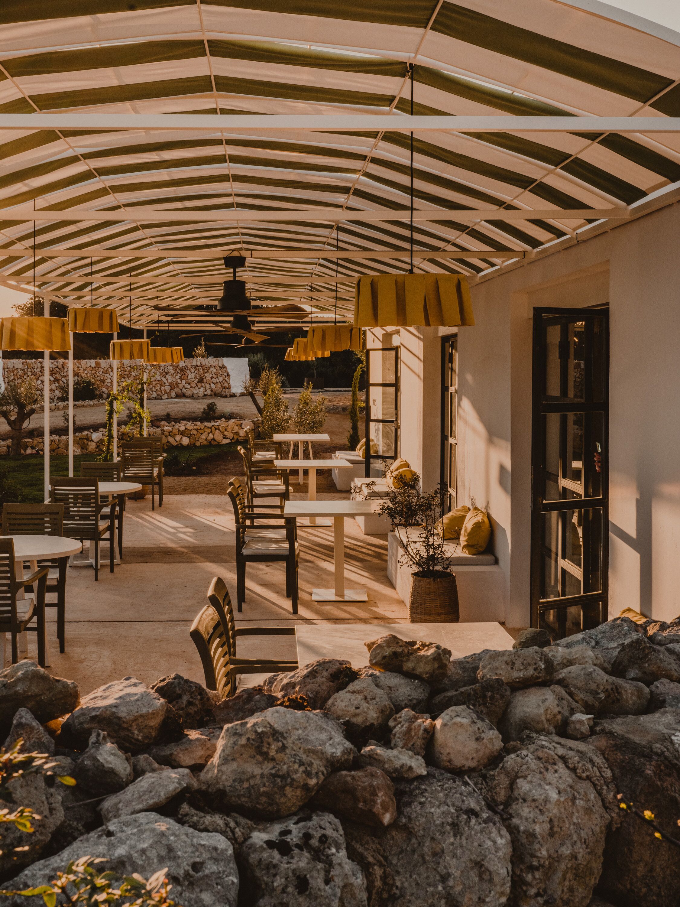 Un espace extérieur aménagé en terrasse, avec des tables et des chaises, un mur en pierre et une grande structure en forme de parasol.