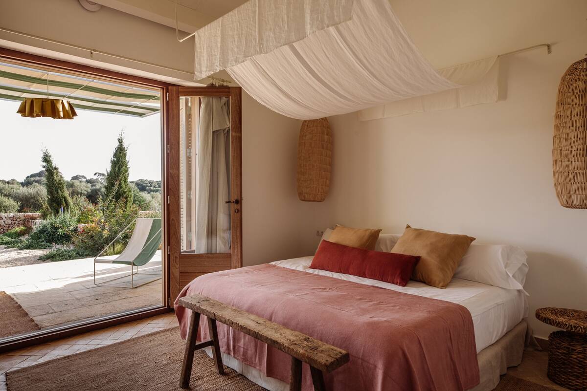 A bedroom with a bed, bench, and a view of the outdoors.