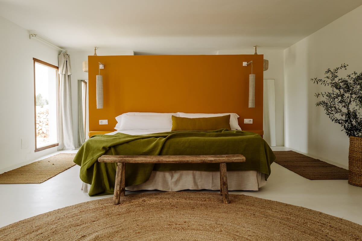 A modern bedroom with a large bed, a bench, and a potted plant.