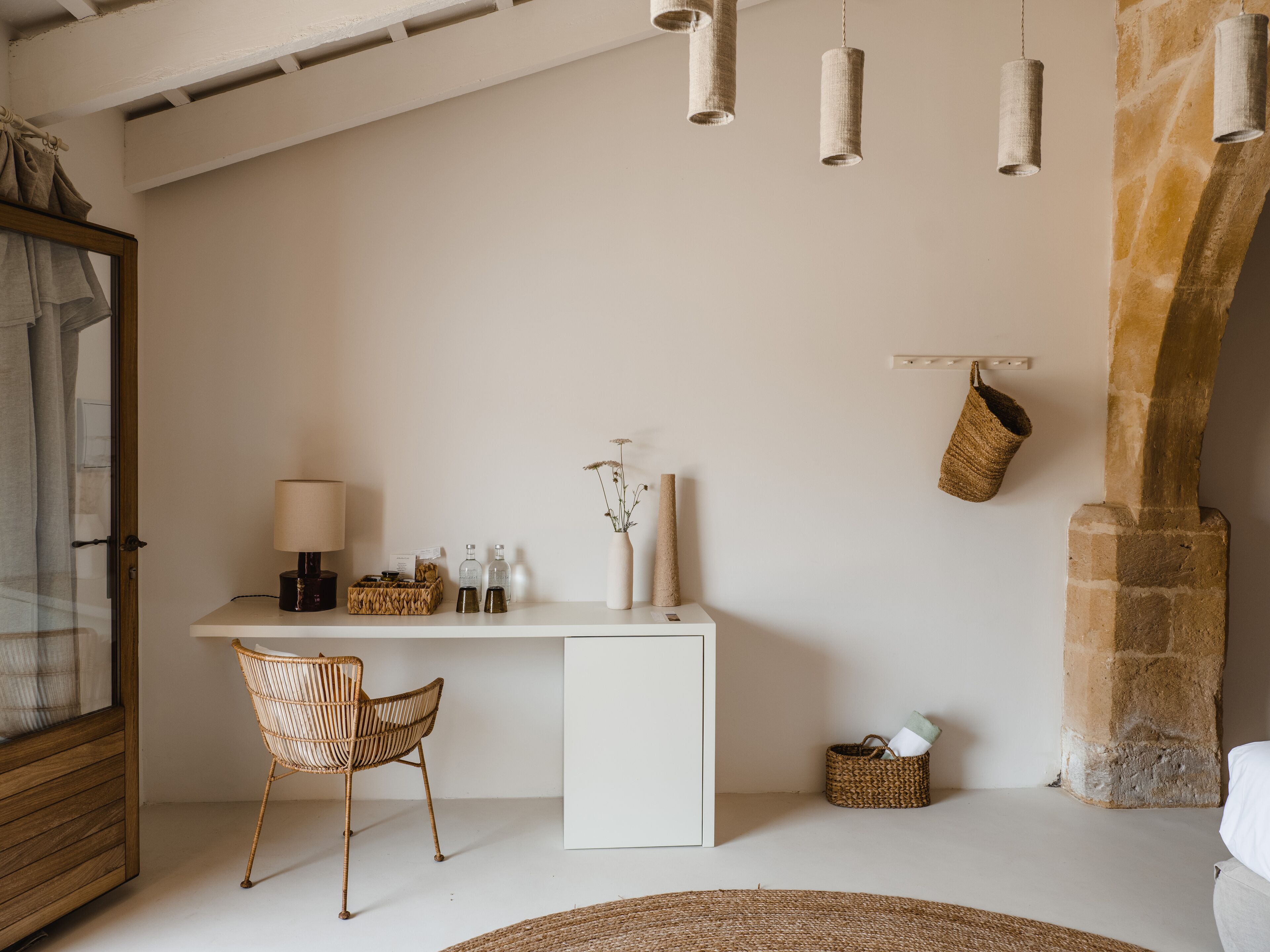 A minimalist room with a white desk, wicker chair, and hanging light fixtures.