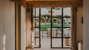 A room with a thatched ceiling, large windows, and a view of a green landscape. - Hotel Amagatay Menorca (Alayor)