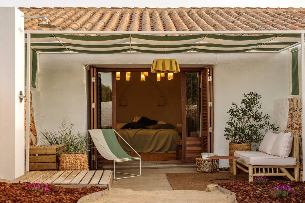 A cozy bedroom with a bed, a green and white striped awning, a wooden bench, and a wicker basket with plants.