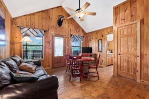 A cozy room with a wooden interior, a leather couch, a dining table with chairs, and a ceiling fan.