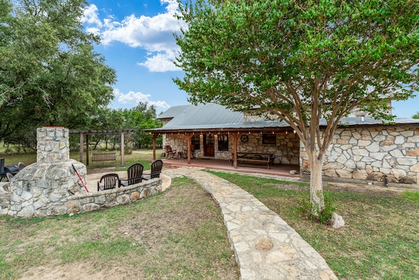 A stone building with a covered patio, outdoor seating, and a stone fireplace.