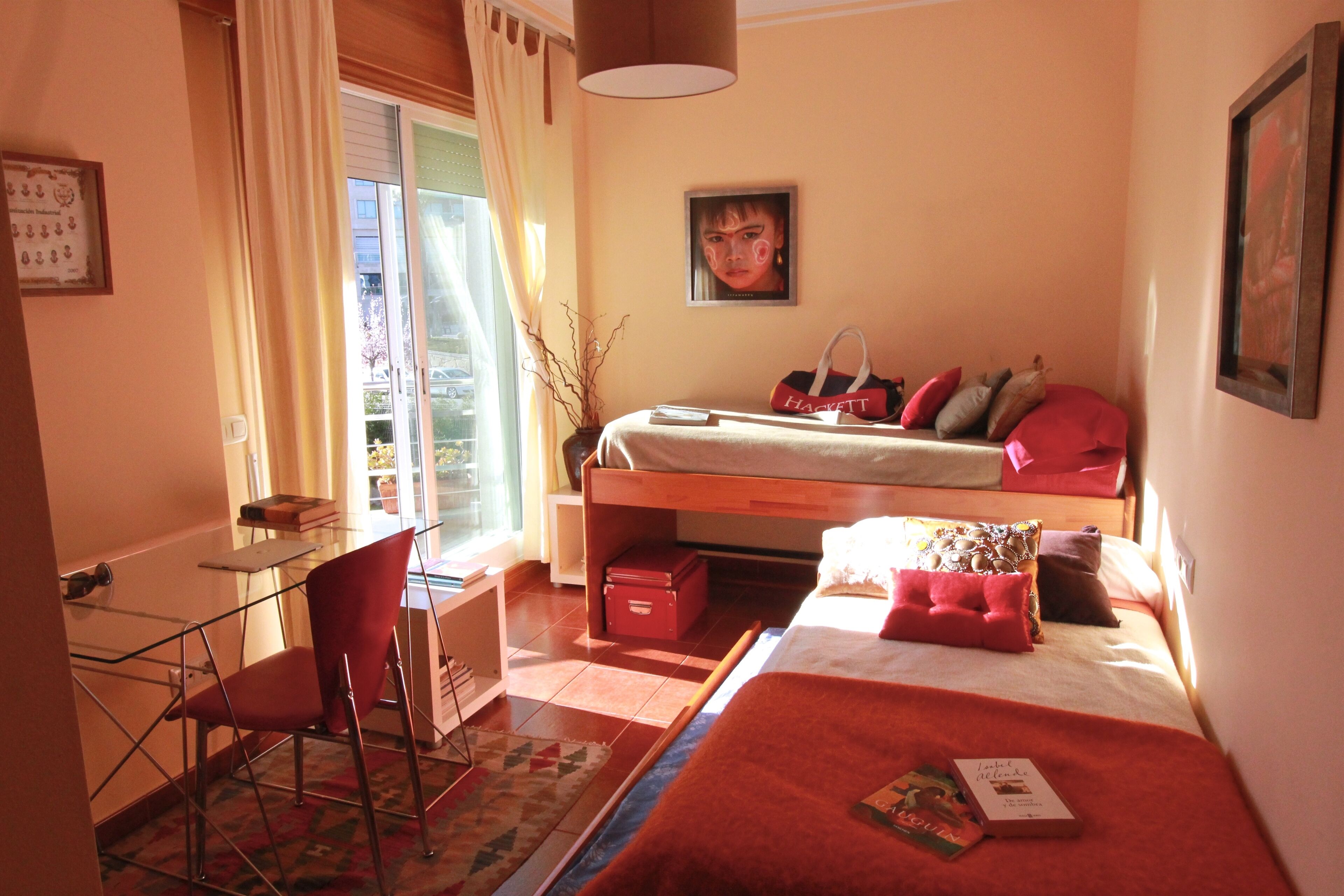 Een slaapkamer met een bed, een bureau en een stoel. Er is een raam met gordijnen, een schilderij aan de muur en een lamp.