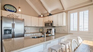 A kitchen with white cabinets, stainless steel appliances, a granite countertop, and a dining area with white chairs.