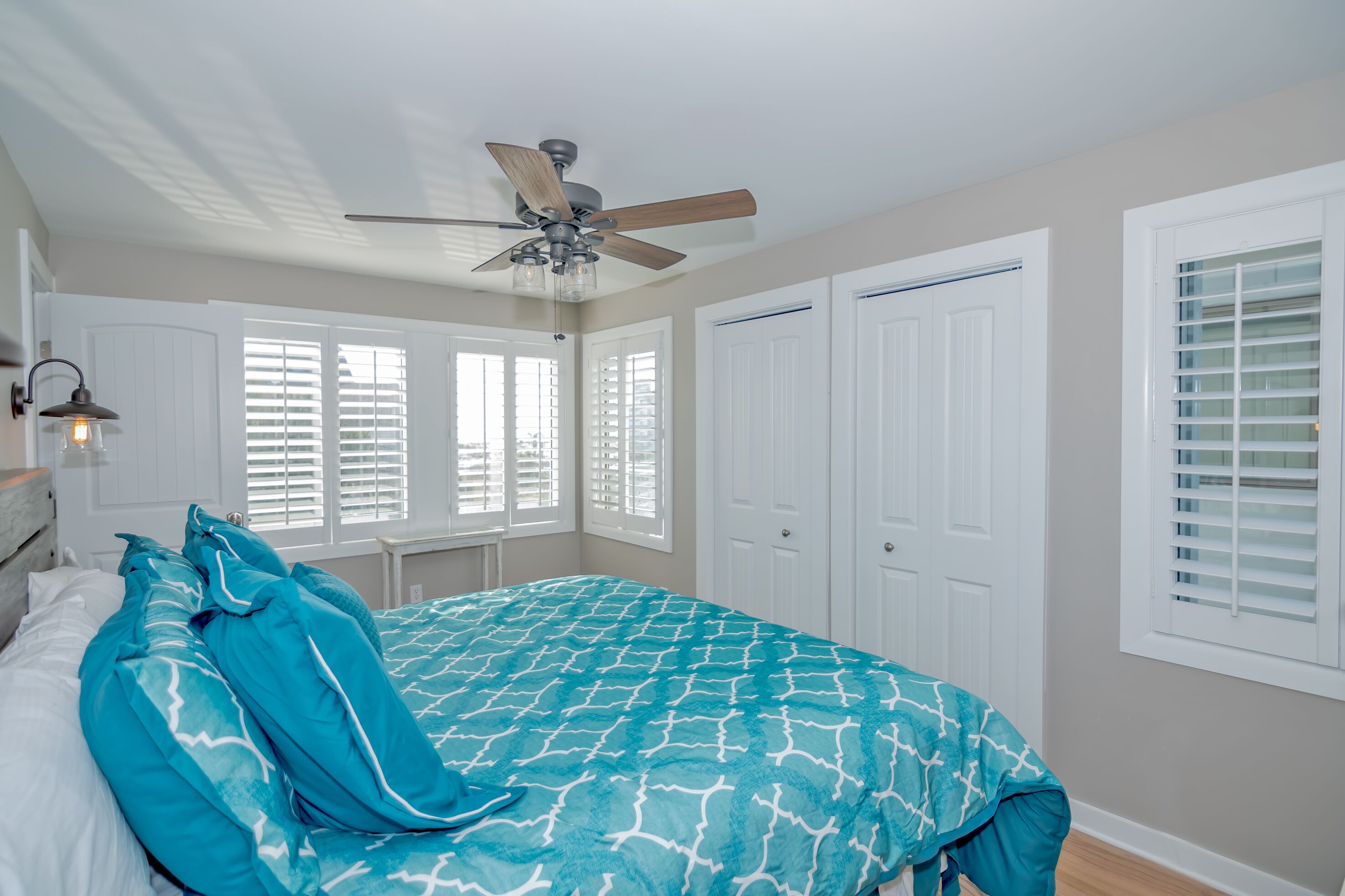 A bedroom with a bed, a ceiling fan, white doors, and windows with blinds.