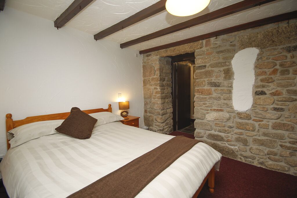 Una camera da letto con parete in pietra, struttura letto in legno e comodino con lampada.