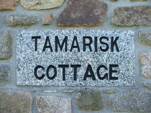 Una targa in pietra con la scritta 'Tamarisk Cottage' su un muro di pietra.