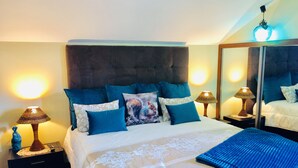A neatly made bed with a headboard, multiple pillows, and a blue throw blanket. There are two bedside tables with lamps, and a large mirror on the wall.