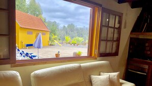A room with a beige sofa, a window with a view of a yellow building and outdoor furniture, and a wooden cabinet.