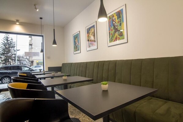 A modern interior with a green upholstered bench, black tables, and pendant lighting.
