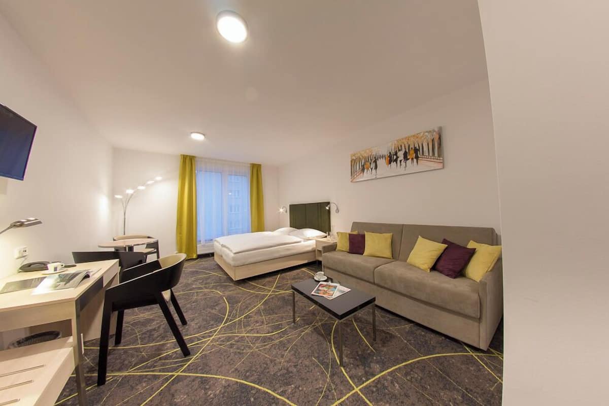 A hotel room with a bed, a sofa, a desk, and a chair.