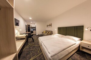 Quarto de hotel com cama, escrivaninha, cadeira e uma pequena cozinha.