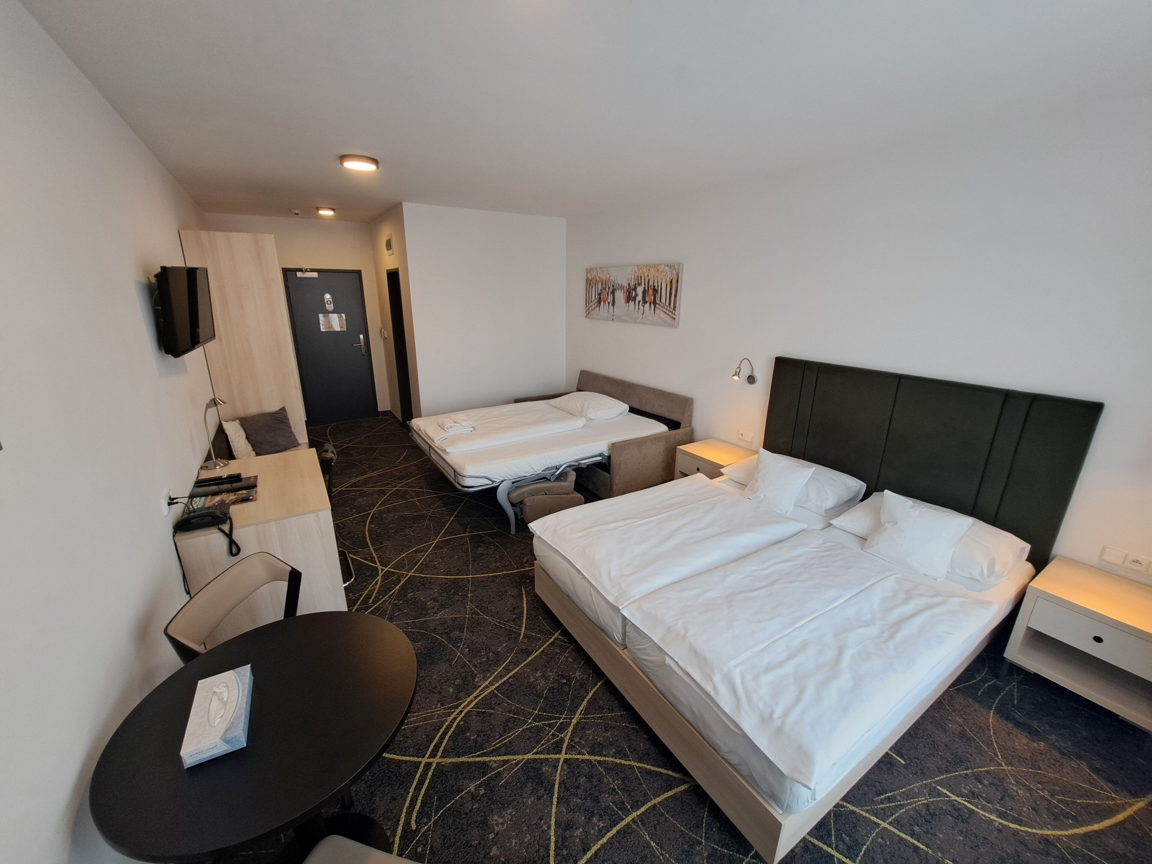 Une chambre d’hôtel avec deux lits, un bureau, une chaise, une télévision et un tableau au mur.