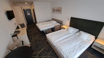 A hotel room with two beds, a desk, a chair, a TV, and a door.