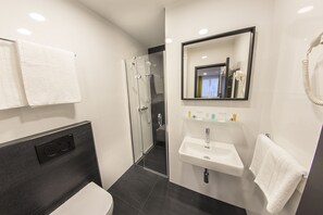Un baño moderno con ducha de vidrio, un lavamanos blanco y un espejo encima.