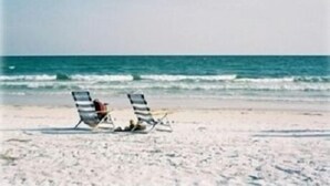 Two beach chairs on a sandy beach with the ocean in the background.