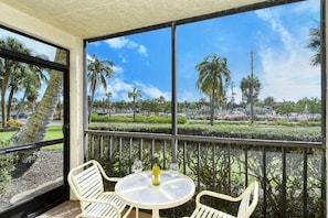 A balcony with a table and chairs, overlooking a landscaped area with palm trees and a clear blue sky.