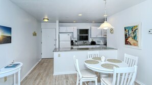 A modern kitchen with white cabinets, a central island, and a dining area with white chairs and a round table.