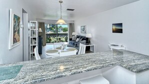 A modern kitchen with granite countertops, a dining area with a round table, and a living room with a sofa and chairs.