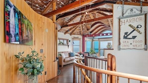 A wooden interior with a wooden staircase, a dining area with a view, and a sign indicating a harbor with seafood and meat. - Whimsical Wave on Miramar Beach | One of a Kind Direct Beachfront Experience! (Santa Barbara)