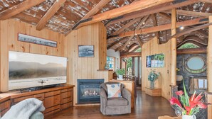 A wooden interior with a fireplace, a television, and a dining area. - Whimsical Wave on Miramar Beach | One of a Kind Direct Beachfront Experience! (Santa Barbara)