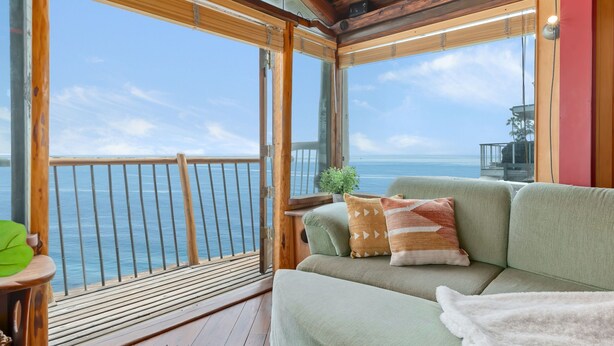 A wooden deck with a cushioned seating area facing a clear view of the ocean. - Whimsical Wave on Miramar Beach | One of a Kind Direct Beachfront Experience! (Santa Barbara)