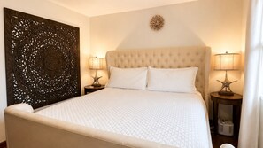 A bedroom with a tufted headboard, two bedside lamps, and a decorative wall panel. - Where Sunsets Dazzle Kihei Oceanfront Corner Condo Sweeping Views and Lanai (Kihei)