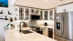 A modern kitchen with white cabinetry, stainless steel appliances, and a built-in microwave. - Where Sunsets Dazzle Kihei Oceanfront Corner Condo Sweeping Views and Lanai (Kihei)
