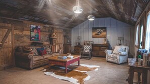 Una sala de estar rústica con un sofá de cuero, una mesa de centro de madera, un sillón estampado y un tapete de piel de vaca.