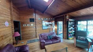 A cozy log cabin interior with a wooden ceiling, a sofa, a coffee table, and a bookshelf. - Lake Shoecraft Waterfront Log Home (Stanwood)
