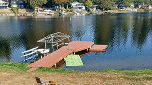 A lakeside deck with a wooden pier, a covered boat dock, and a small seating area with chairs and a table. - Lake Shoecraft Waterfront Log Home (Stanwood)