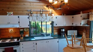 A modern kitchen with white cabinets, a stove, a sink, and a dining area with a wooden table and chairs. - Lake Shoecraft Waterfront Log Home (Stanwood)