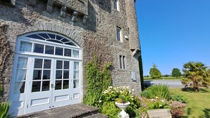 A stone castle with a large arched entrance, steps leading up to a door, and a garden with flowers and a wicker table. - Lisheen Castle, Beautifully Restored, Perfect Central Location for Day Tripping  (Thurles)