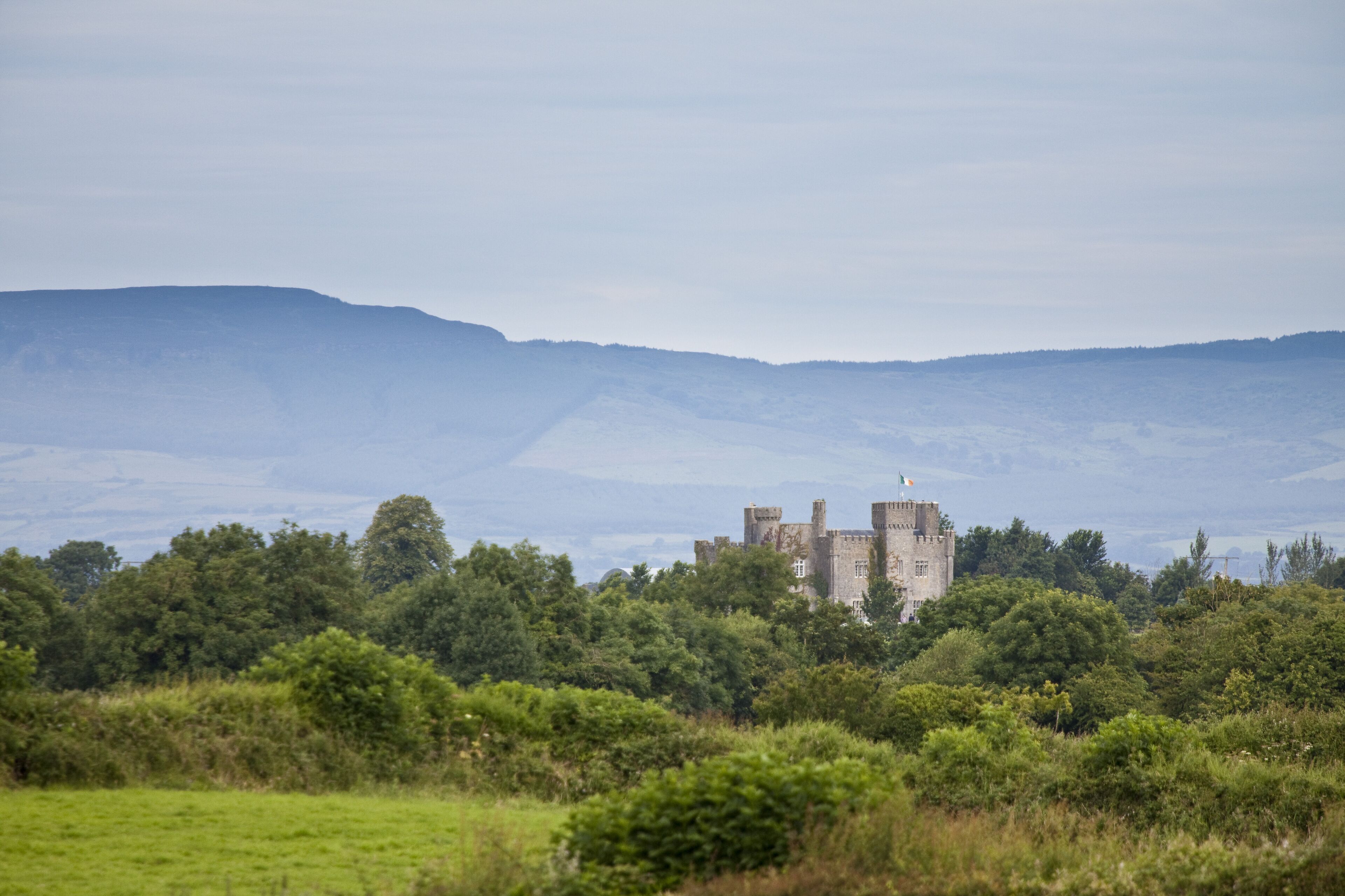 Eine Burg, umgeben von üppigem Grün und Hügeln im Hintergrund.