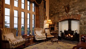 A cozy living room with a fireplace, striped armchairs, and a large window with curtains. - Lisheen Castle, Beautifully Restored, Perfect Central Location for Day Tripping  (Thurles)