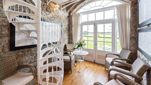 A room with a spiral staircase, wicker furniture, a round table with a vase, and a large window with curtains. - Lisheen Castle, Beautifully Restored, Perfect Central Location for Day Tripping  (Thurles)