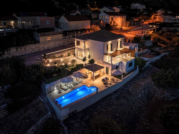 Una casa de dos plantas con piscina, zona de estar exterior y un muro de piedra.