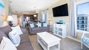 Ein geräumiges Wohnzimmer mit grauem Sofa, weißem Couchtisch und einem an der Wand befestigten Fernseher.