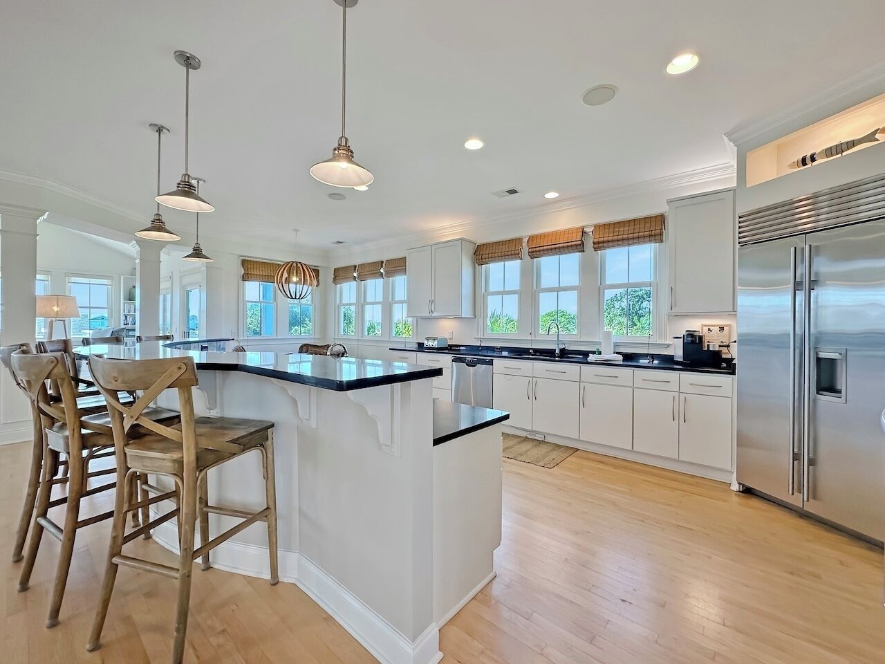 A modern kitchen with a central island, bar stools, pendant lighting, and a stainless steel refrigerator.