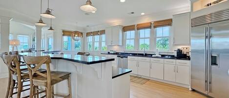 Cozinha moderna com ilha central, banquetas, iluminação pendente e geladeira de aço inoxidável.